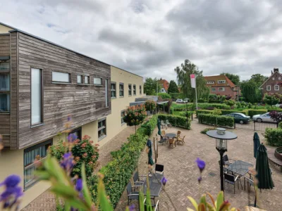 Buitenaanzicht van woonzorglocatie De Houttuinen, met rechts op de foto een terras met tafels en stoelen.